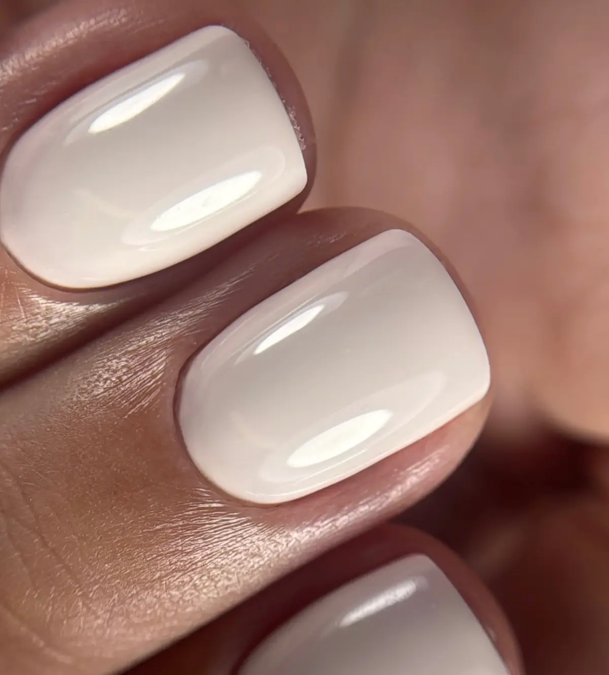 Unhas curtas em gel branco leitoso, com brilho e cutícula bem feita.