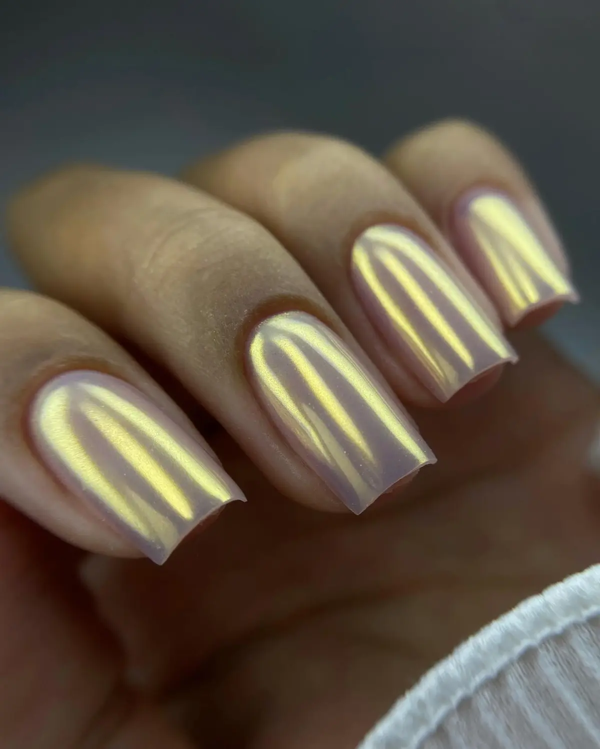 Unhas quadradas com efeito cromado perolado em tons de dourado.