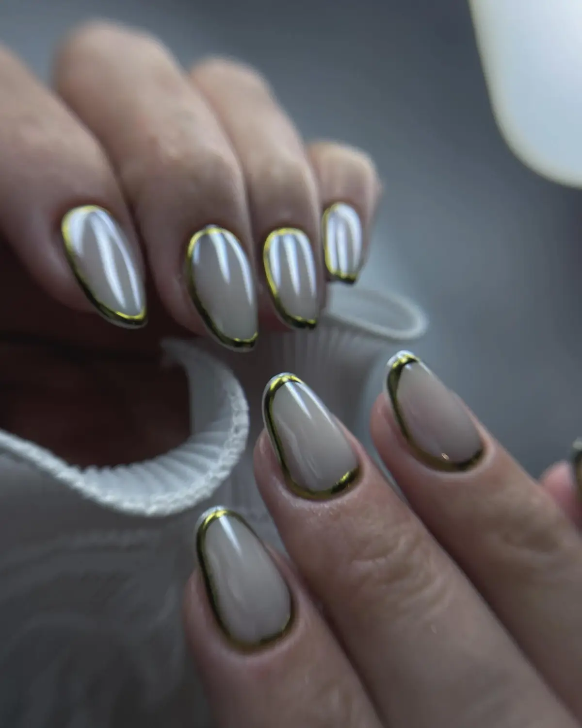 Unhas amendoadas em tom nude, com um contorno fino dourado.